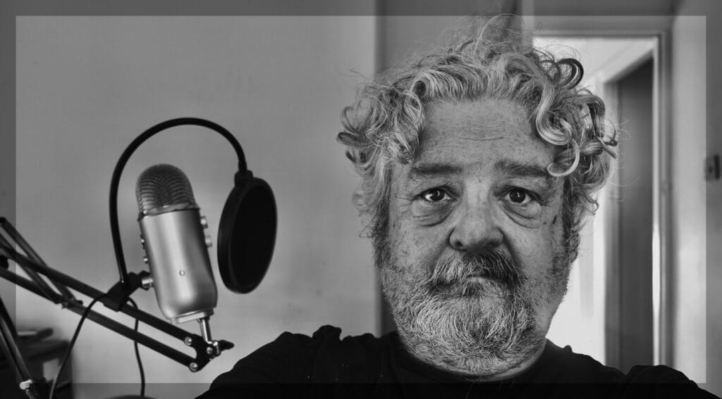 A very hirsute author with a microphone to his right.