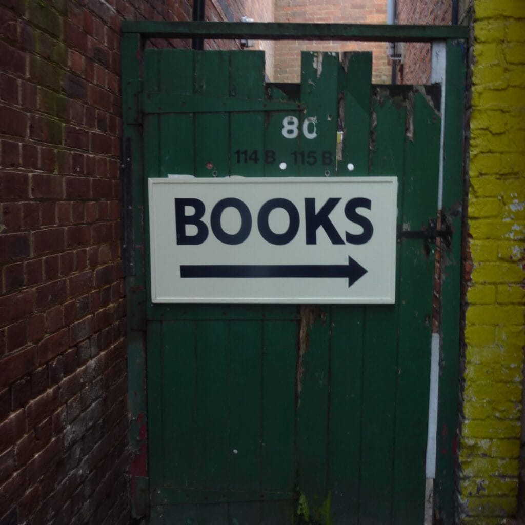 A white sign with black text ("Books") with an arrow pointing right to left.