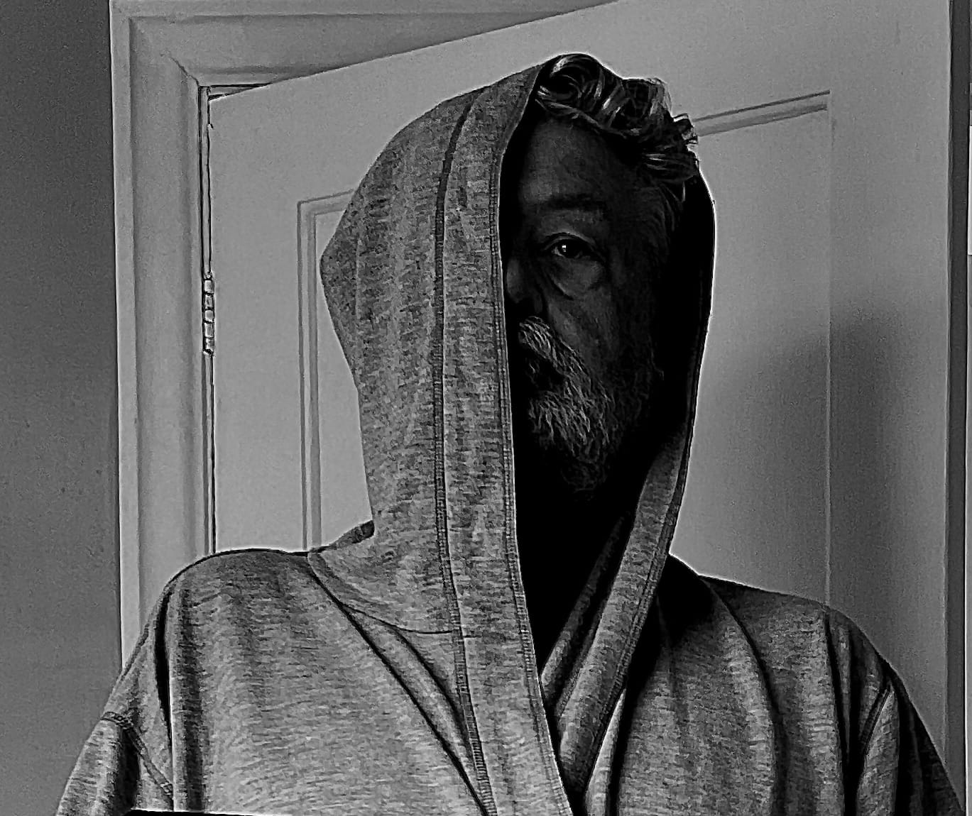 A hooded figure, bearded, hooded, stares at you.